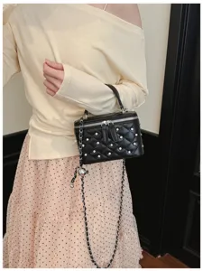 Close-up of black quilted box bag featuring pearl studs and elegant silver chain strap