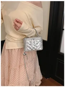 Macro view of a stylish silver quilted box handbag featuring pearls and rhinestone details.