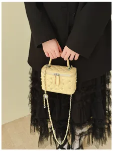 Close-up of a yellow quilted vanity bag featuring elegant pearl and rhinestone details.