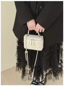 Detail of cream quilted vanity bag with pearl accents and chain strap held by model