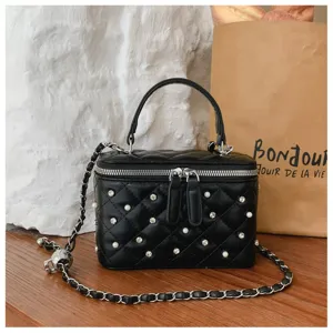 Close-up of black quilted vanity bag with pearls and rhinestones on wooden table.