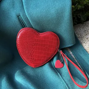 Detail of red heart-shaped coin purse with crocodile texture on teal fabric background