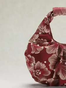 Dettaglio di una borsa a mano plissettata in jacquard rosso con perle bianche delicate.