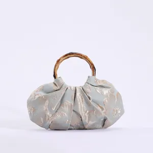 Detailopname van de retro geplooide stoffen handtas met een natuurlijk bamboe handvat.