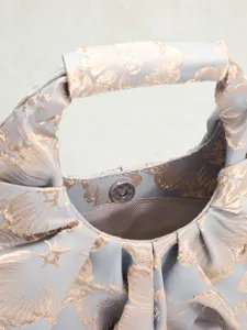 Vista dettagliata del tessuto jacquard floreale dorato e chiusura magnetica su borsa a pieghe