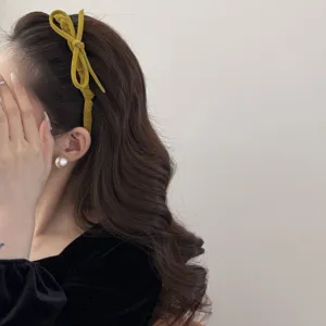Close-up of a mustard yellow flocked bow headband worn on elegant brown wavy hair