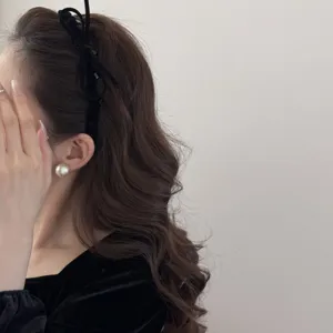 Close-up detail of a black velvet bow headband styled on wavy brown hair for a retro look.
