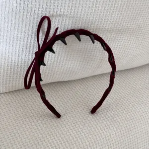Close-up of a stylish burgundy velvet headband featuring a side bow and black decorative spikes.
