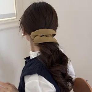 Detalle de un gran coletero de tela amarillo mostaza en una coleta baja de pelo castaño.