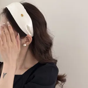 Retro wide white fabric headband with small gold label for high skull top hair styling.