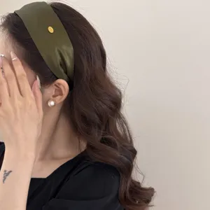 Detail shot of a stylish olive green wide headband with a vintage gold label on hair.