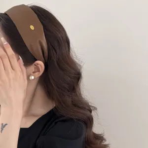 Close-up detail of a wide brown retro headband with a small gold label on long wavy hair