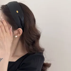 Side view detail of a vintage black wide headband featuring a stylish gold label on a model