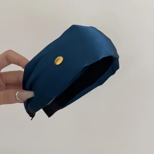 Detailed view of a navy blue wide headband featuring a gold 'SMILE HAPPY' metal tag.