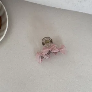Close-up of a elegant pink mesh bow hair claw clip on a neutral textured surface.