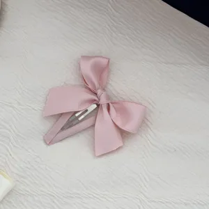 Primo piano di un fermaglio per capelli con fiocco rosa satinato su tessuto bianco.