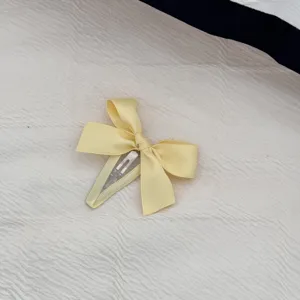 Dettaglio di una dolce molletta per capelli con fiocco giallo su tessuto bianco