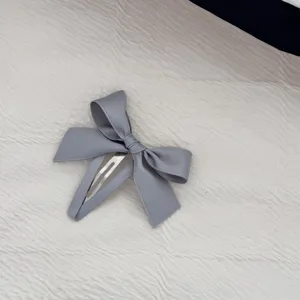 Dettaglio di un fermaglio per capelli a fiocco grigio con clip a scatto in metallo.