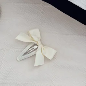Dettaglio di un'elegante molletta per capelli con fiocco color crema su tessuto