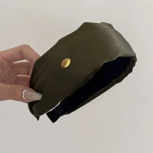 Close-up detail of a vintage olive green wide satin headband with a gold SMILE label.