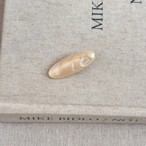 Gros plan d'une pince à cheveux ovale en acétate beige avec texte France Handmade
