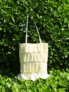 Multi-layer pleated ruffle tote bag in cream yellow against green garden background