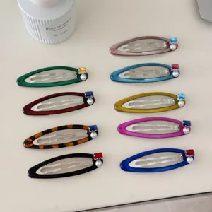 Vue détaillée de diverses barrettes à cheveux colorées avec perles et zircons sur un bureau blanc.