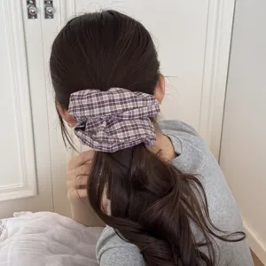 Detail view of a purple checkered fabric scrunchie holding a wavy ponytail hair style.