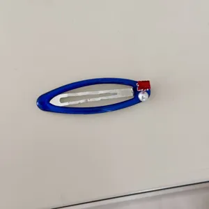 Détail d'une pince à cheveux BB bleue avec zircon rouge et perle sur fond neutre