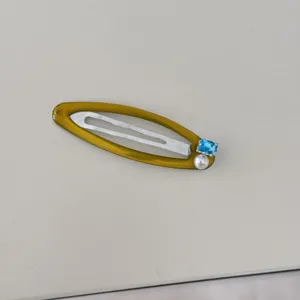 Détail d'une barrette dorée ornée d'un zircon bleu carré et d'une perle blanche ronde.