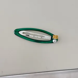Vue détaillée d'une barrette verte ornée de zircon jaune et d'une perle blanche.
