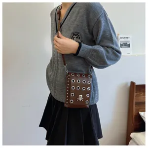 Close-up of a brown gothic crossbody bag with silver eyelets and a metal skull emblem