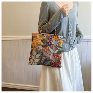 Close-up of elegant linen handbag with colorful floral embroidery and bamboo handle