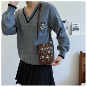 Detail of a brown gothic crossbody bag featuring silver eyelets and a skull cross charm.