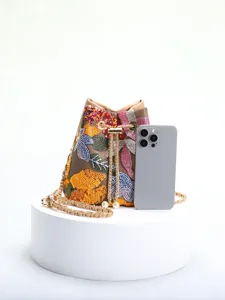 Size comparison of floral embroidered bucket bag with a smartphone on white pedestal