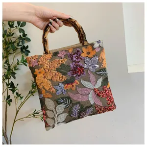 Detail view of linen evening bag with colorful floral embroidery and bamboo handle
