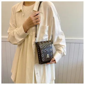 Dark gothic crossbody bag with skull ornament and metal grommets on a beige outfit