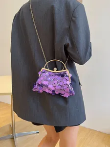 Elegante lila Pailletten-Abendtasche mit Metallgriff, getragen über einem grauen Blazer.