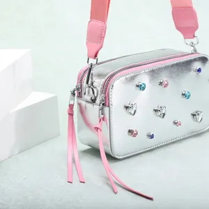 Primer plano de bolso de cámara plateado metálico con pedrería de colores y rosa