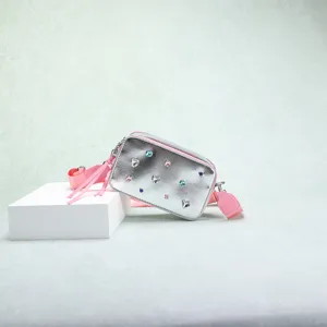 Primer plano de un bolso de cámara plateado con pedrería de colores y detalles de borlas