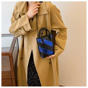 Detailed view of striped blue and black bucket bag worn over a beige trench coat