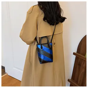 Detail of a small striped bucket bag in blue and black worn with a beige coat