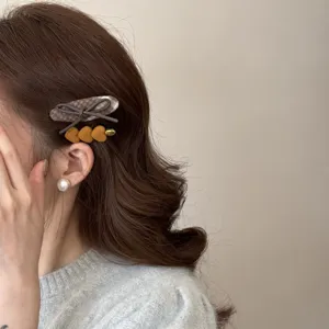 Close-up of retro plaid bow and yellow heart hair clips styled on wavy brown hair