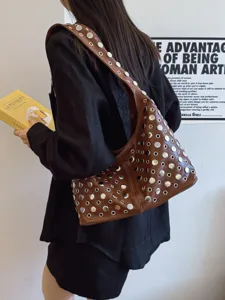 Trendy brown shoulder bag with silver rivets carried by a model in a stylish outfit.