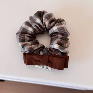 Detailed macro view of a vintage plaid hair scrunchie featuring a brown fabric bow
