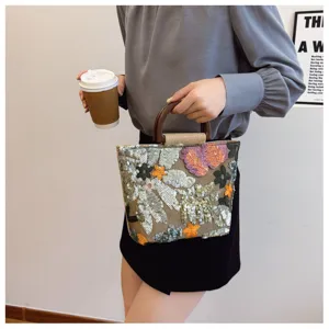 Dettaglio di una borsa in lino con paillettes floreali e manico in bambù vintage.