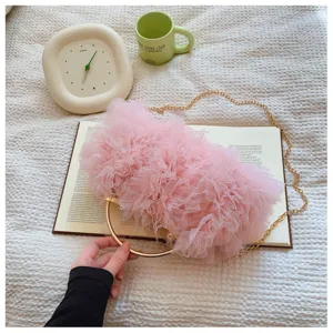 Elegant pink ruffled tulle evening clutch bag with gold ring handle in a lifestyle setting.