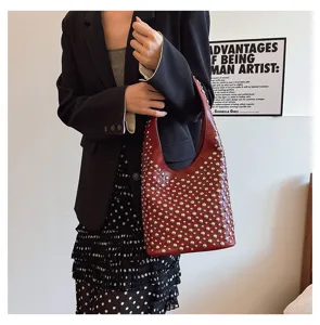 Close-up of a punk style burgundy bucket bag with silver studs worn by a model