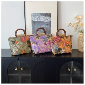 Tre borse in lino con paillettes floreali e manici in legno su un mobile nero.