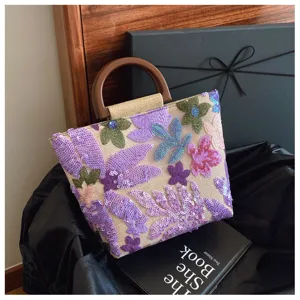 Borsa in lino con ricamo floreale di paillettes e manico tondo in legno pregiato.